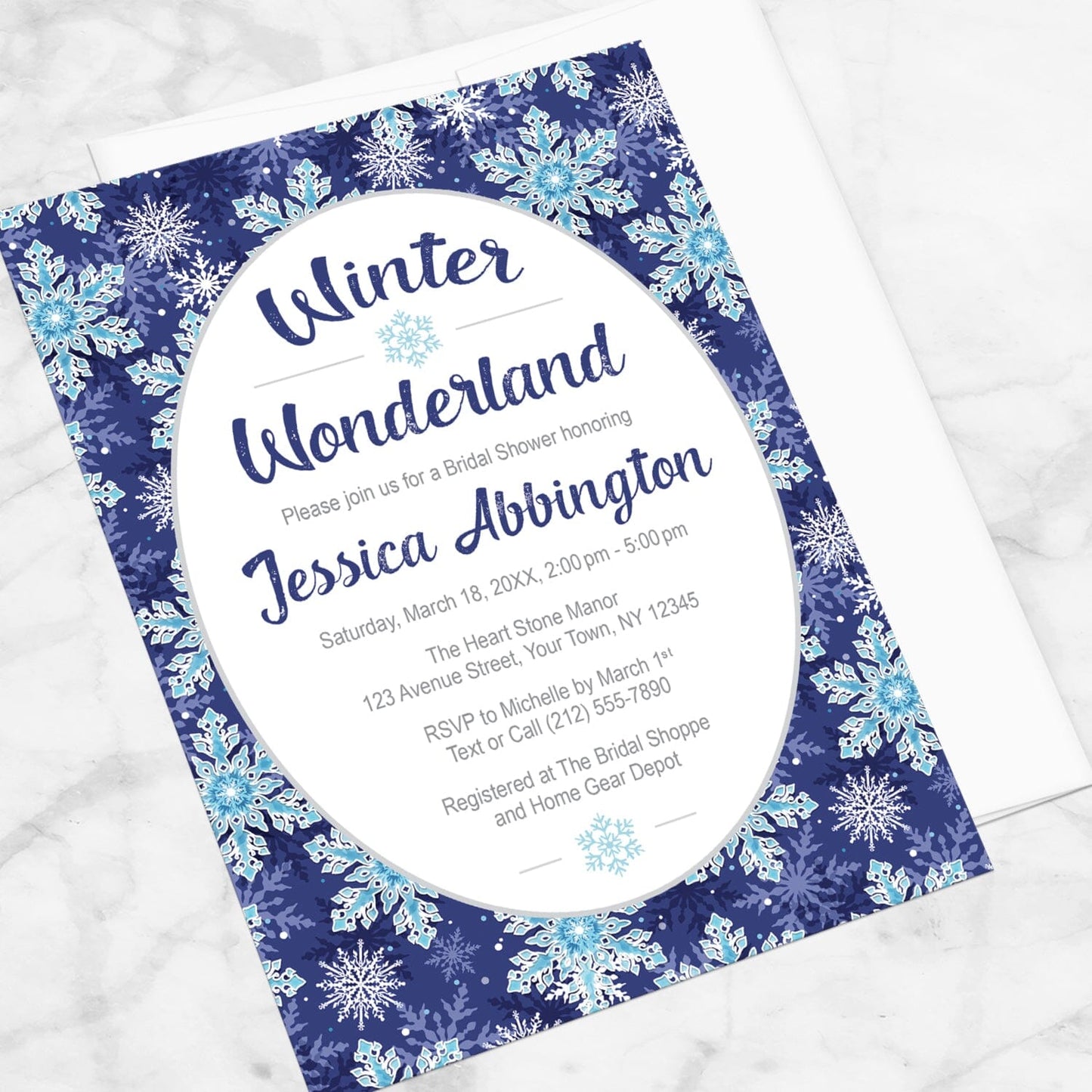 Winter Wonderland bridal shower invitation with a navy blue snowflake design shown at an angle on a marble surface with a white envelope.