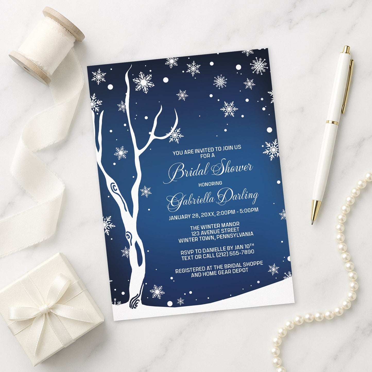 Navy Night Sky Snowflake Winter Bridal Shower Invitation shown on a marble surface with a white gift box, pen, ribbon, and pearls.