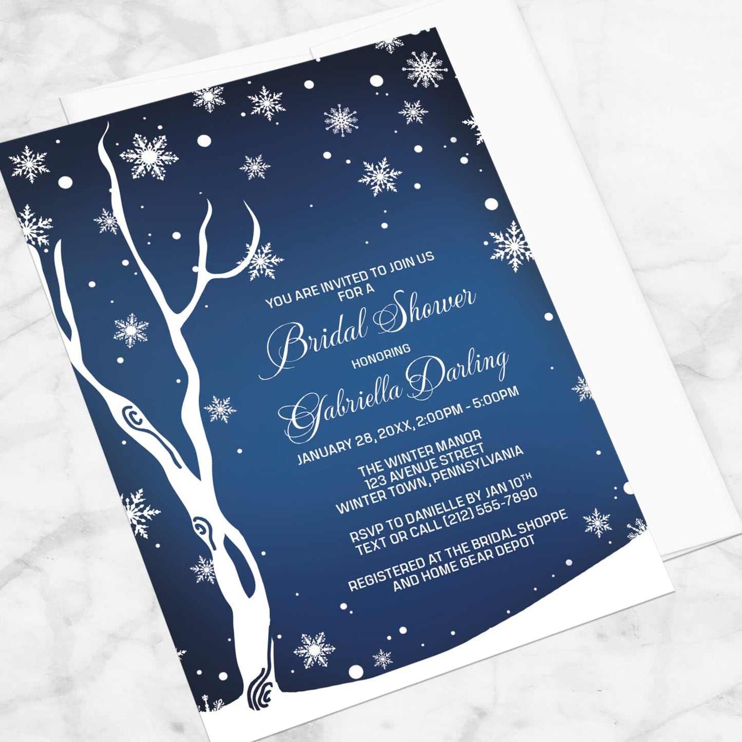 Navy Night Sky Snowflake Winter Bridal Shower Invitation shown at an angle on a marble surface with a white envelope.