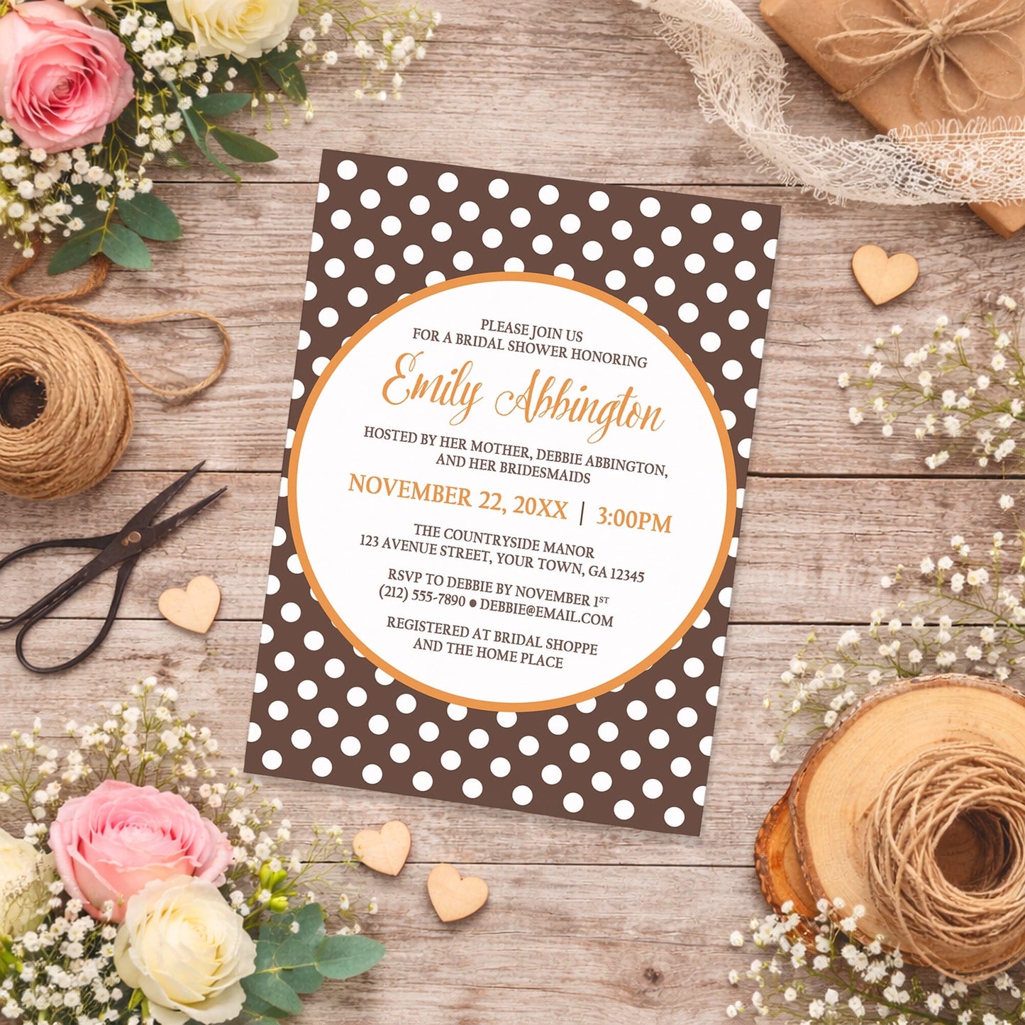 Orange Brown Polka Dot Bridal Shower Invitation on a rustic wood surface with flowers and twine.