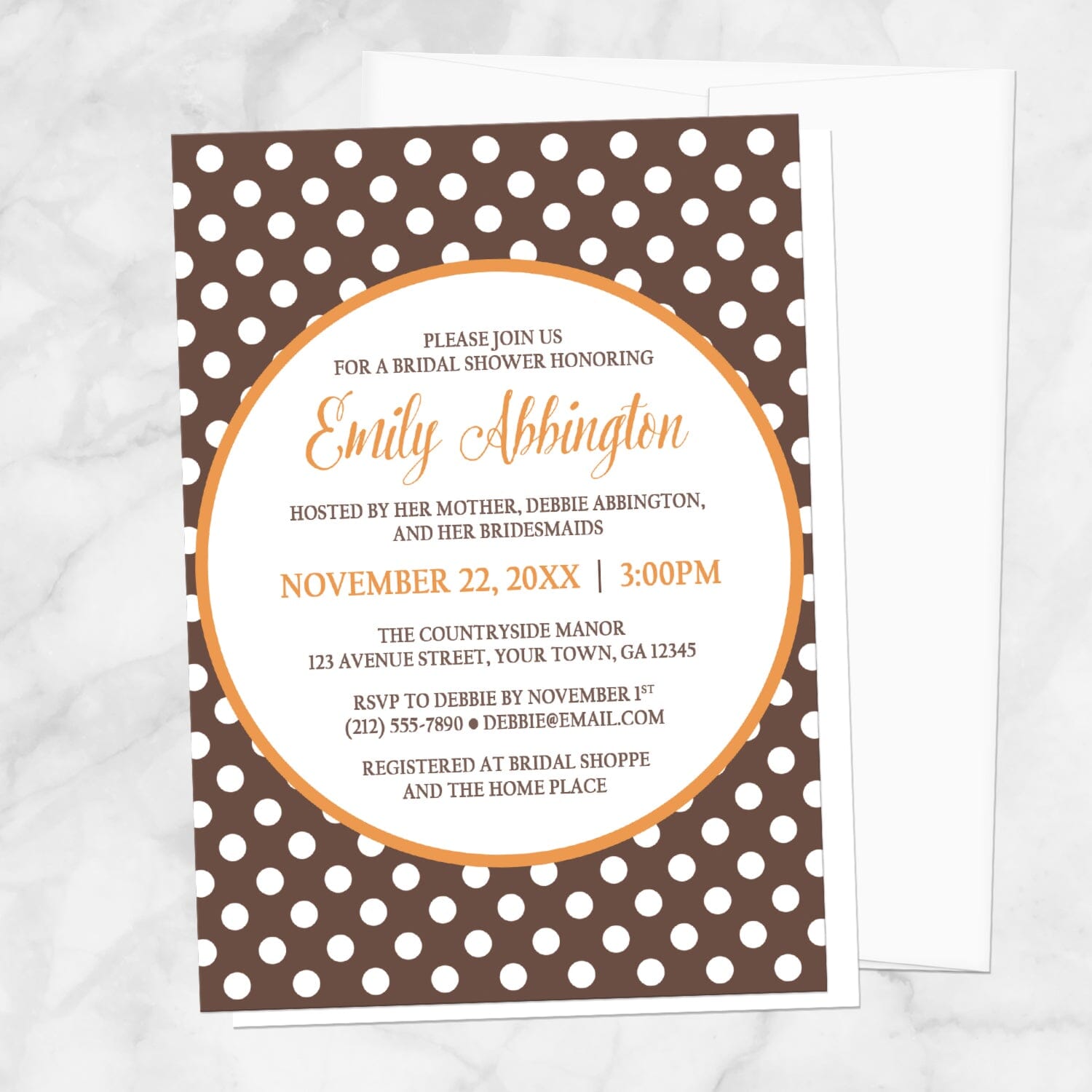 Bridal Shower invitation with a brown polka dot pattern and orange accents, displayed with a white envelope on a marble surface