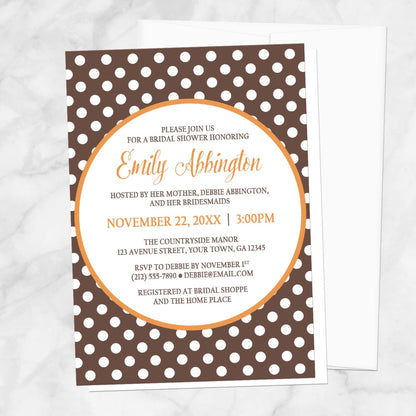 Bridal Shower invitation with a brown polka dot pattern and orange accents, displayed with a white envelope on a marble surface
