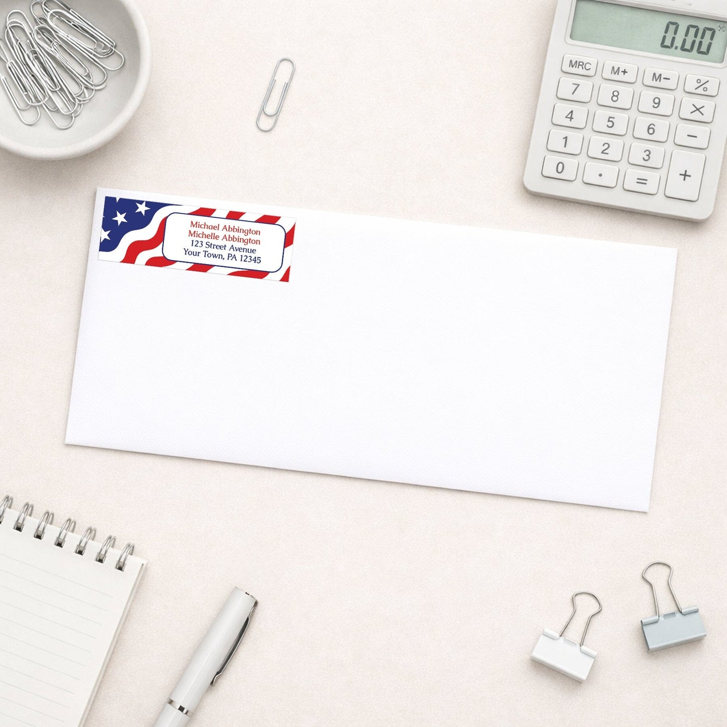 Envelope with address label featuring an American flag design on a desk with office supplies.