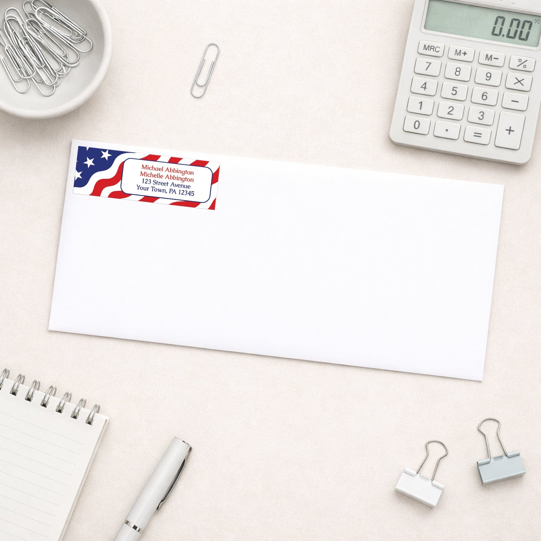 Envelope with address label featuring an American flag design on a desk with office supplies.
