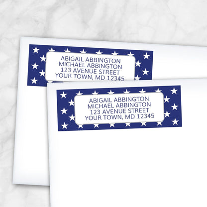 Two address labels with a blue border featuring white stars, shown on white envelopes, on a marble surface.