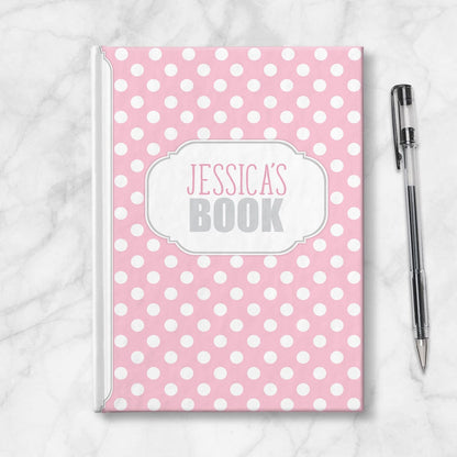 Personalized Pink Polka Dot Journal at Artistically Invited. Image shows the book on a countertop with a pen next to it.