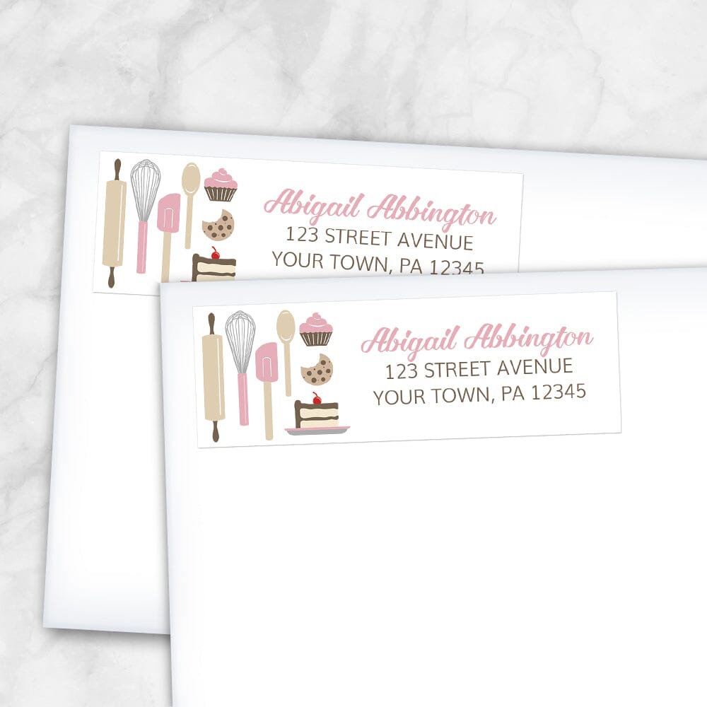 Pink Baking Address Labels at Artistically Invited. Image shows 2 labels on envelopes. High-quality address labels designed with cute kitchen baking tools and baked treats in pink, brown, gray, and beige on the left side over a white background. Your personalized return address is custom printed in pink and brown to the right of the pink baking tools and baked goods design. These premium return address labels are great for bakers, pastry chefs, or anyone who loves baking.