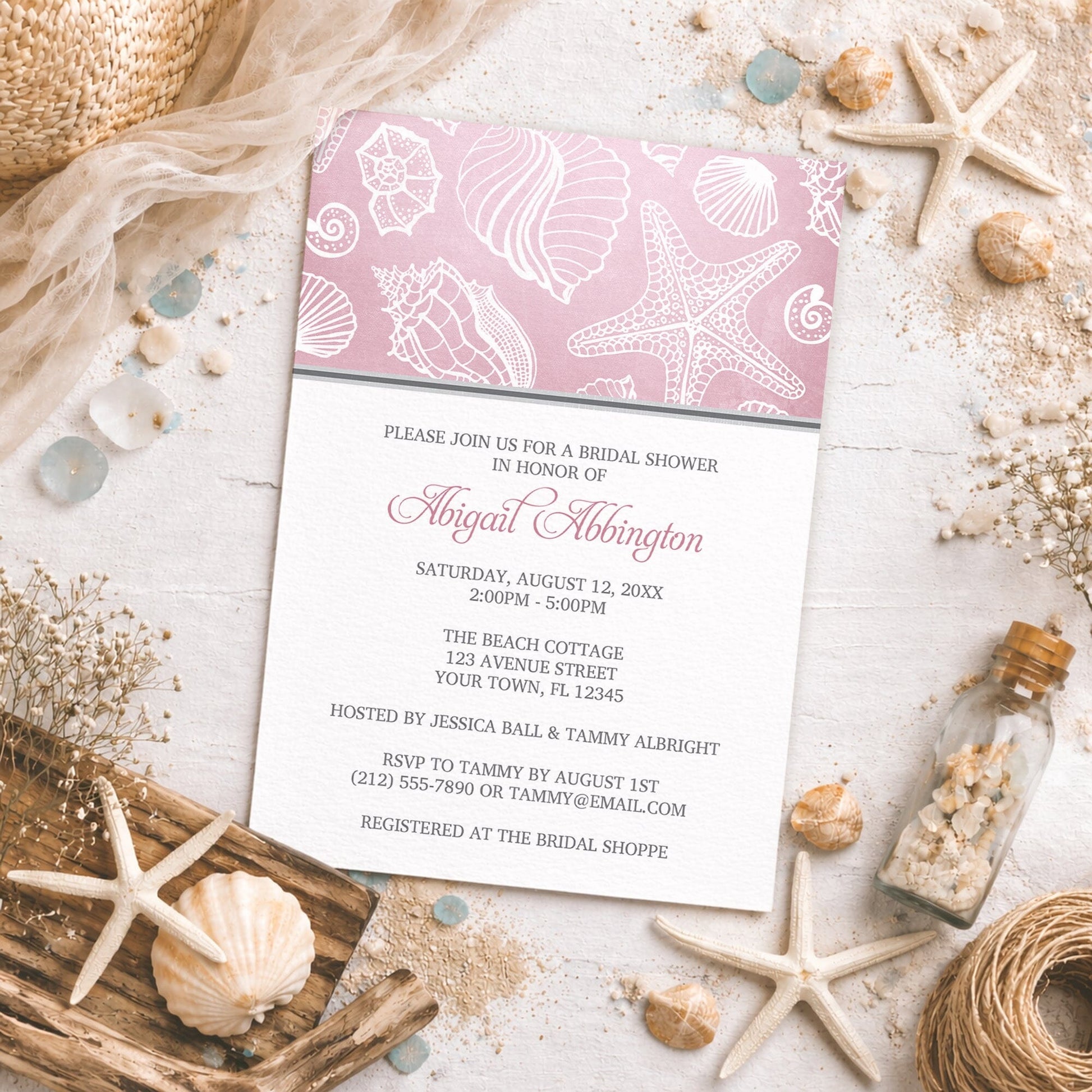 Pink Beach Seashell Pattern Bridal Shower Invitation shown on a beachy surface with sand and coastal decor.