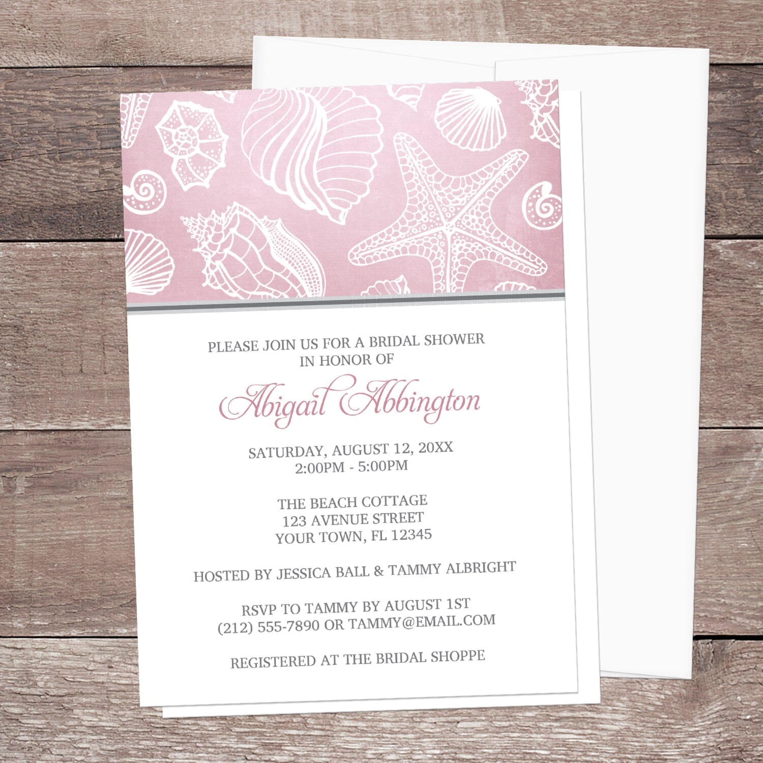 Pink Beach Seashell Pattern Bridal Shower Invitation shown on a wooden surface with a white envelope.