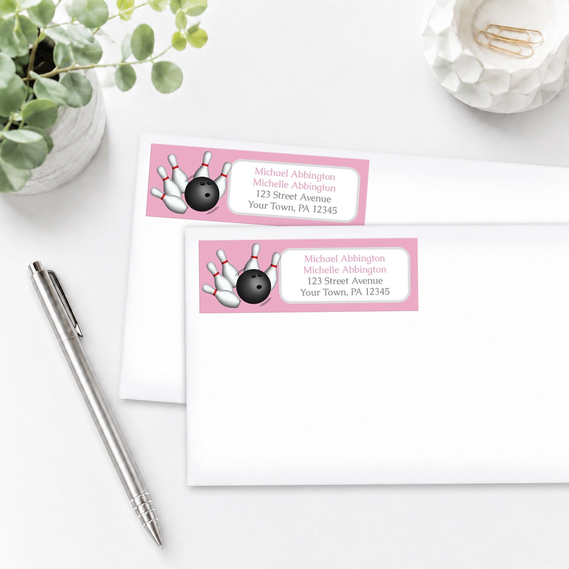 Pink Bowling Address Labels on white envelopes, shown on a white surface with a plant and a pen.