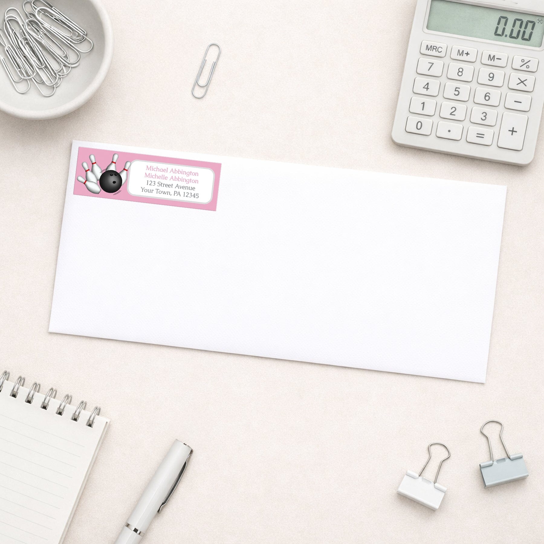 Pink Bowling Return Address Label shown on a white envelope with everyday office supplies