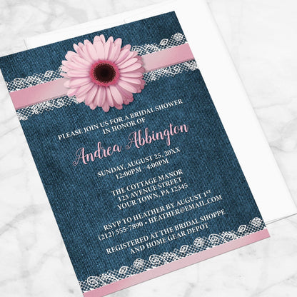 Bridal shower invitation with a pink daisy, denim and lace, displayed at an angle with a white envelope on a marble surface