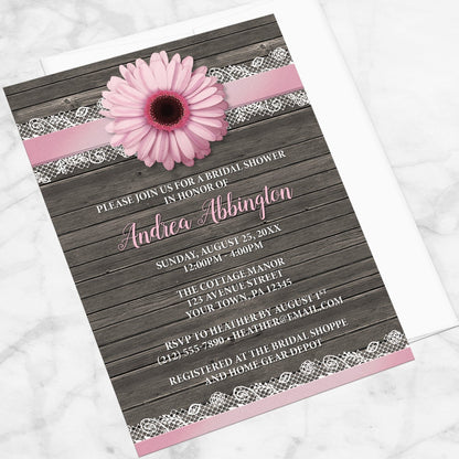 Pink Daisy Lace Rustic Wood Bridal Shower Invitation shown at an angle on a marble surface with a white envelope.