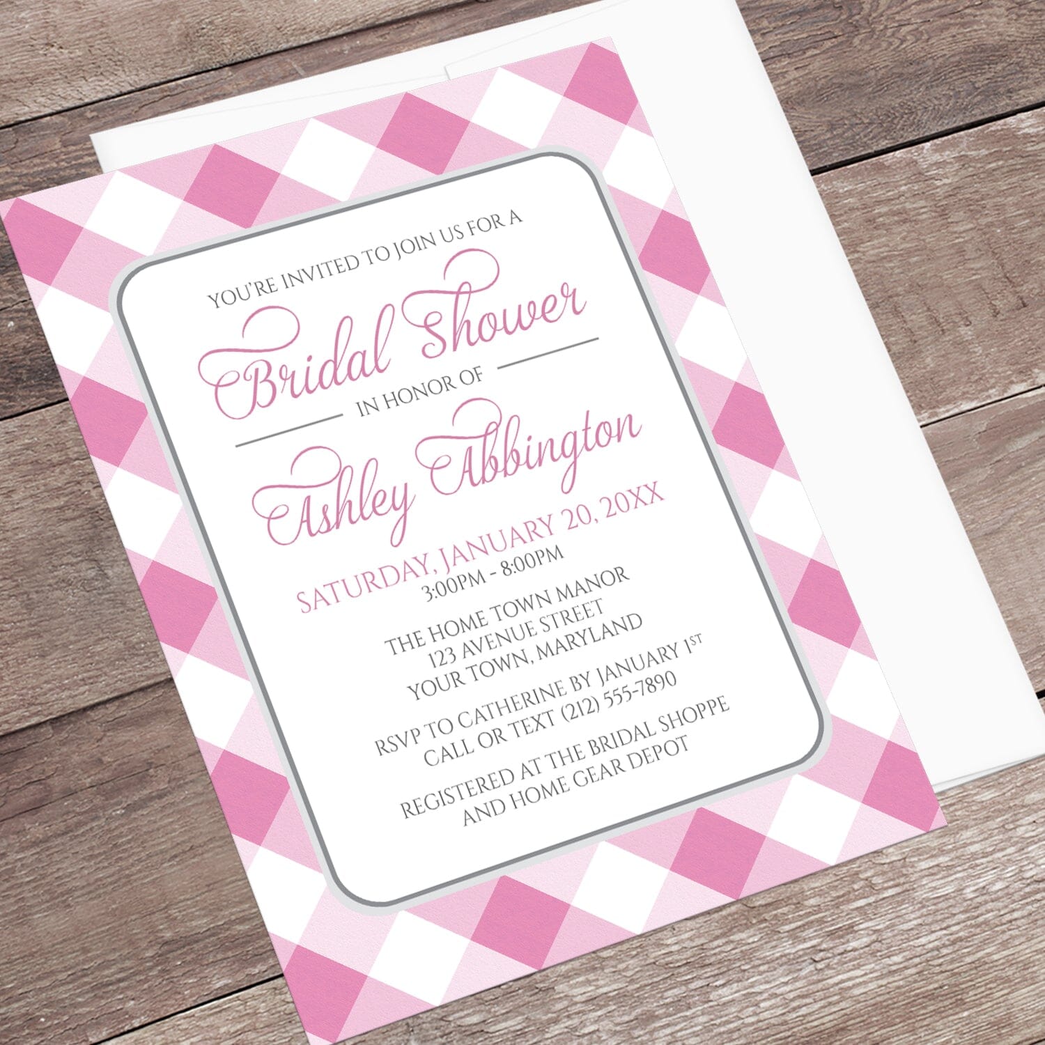 Pink Gingham Bridal Shower Invitation shown at an angle on a wooden surface with a white envelope.