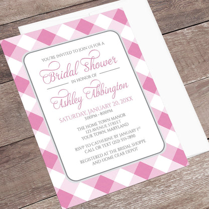Pink Gingham Bridal Shower Invitation shown at an angle on a wooden surface with a white envelope.