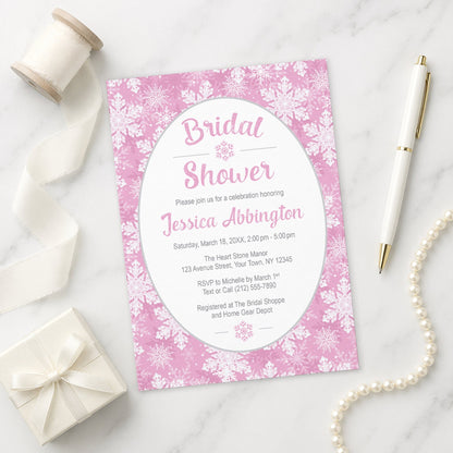 Pink Snowflake Bridal Shower Invitation shown on a marble surface with a white gift box, pen, ribbon, and pearls.