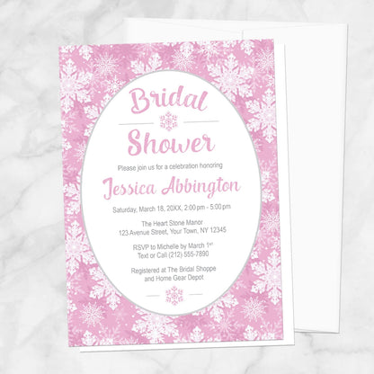 Pink Snowflake Bridal Shower Invitation shown on a marble surface with a white envelope.