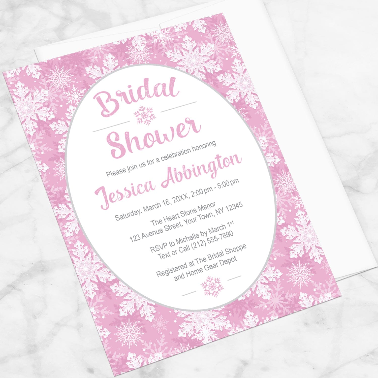 Pink Snowflake Bridal Shower Invitation shown at an angle on a marble surface with a white envelope.