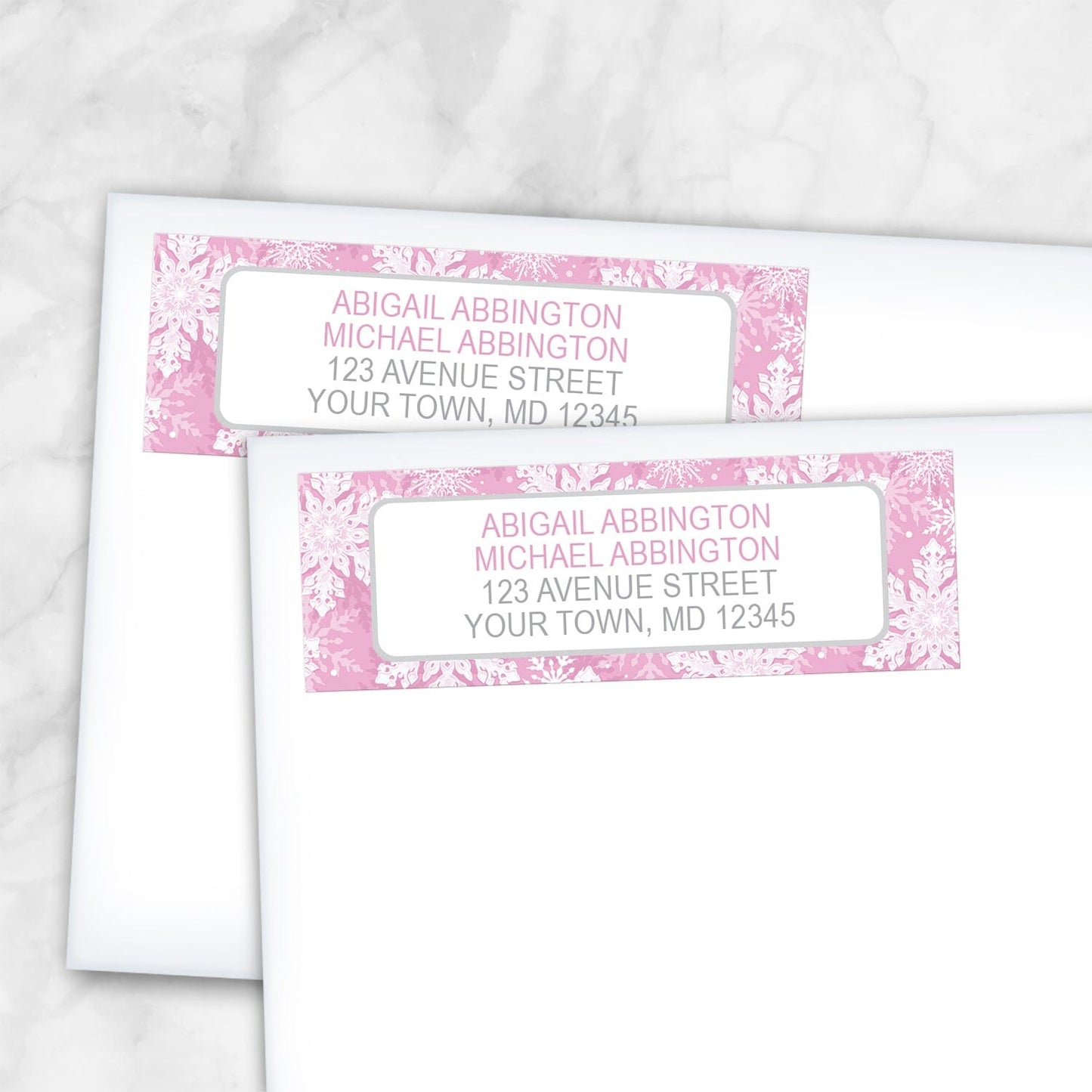 2 Pink Snowflake Winter Return Address Labels shown on white envelopes on a marble surface