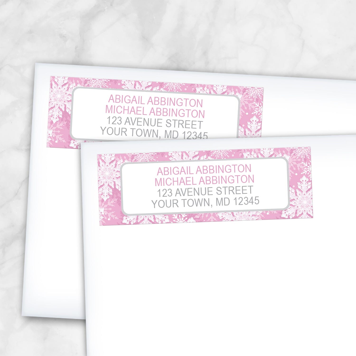 2 Pink Snowflake Winter Return Address Labels shown on white envelopes on a marble surface