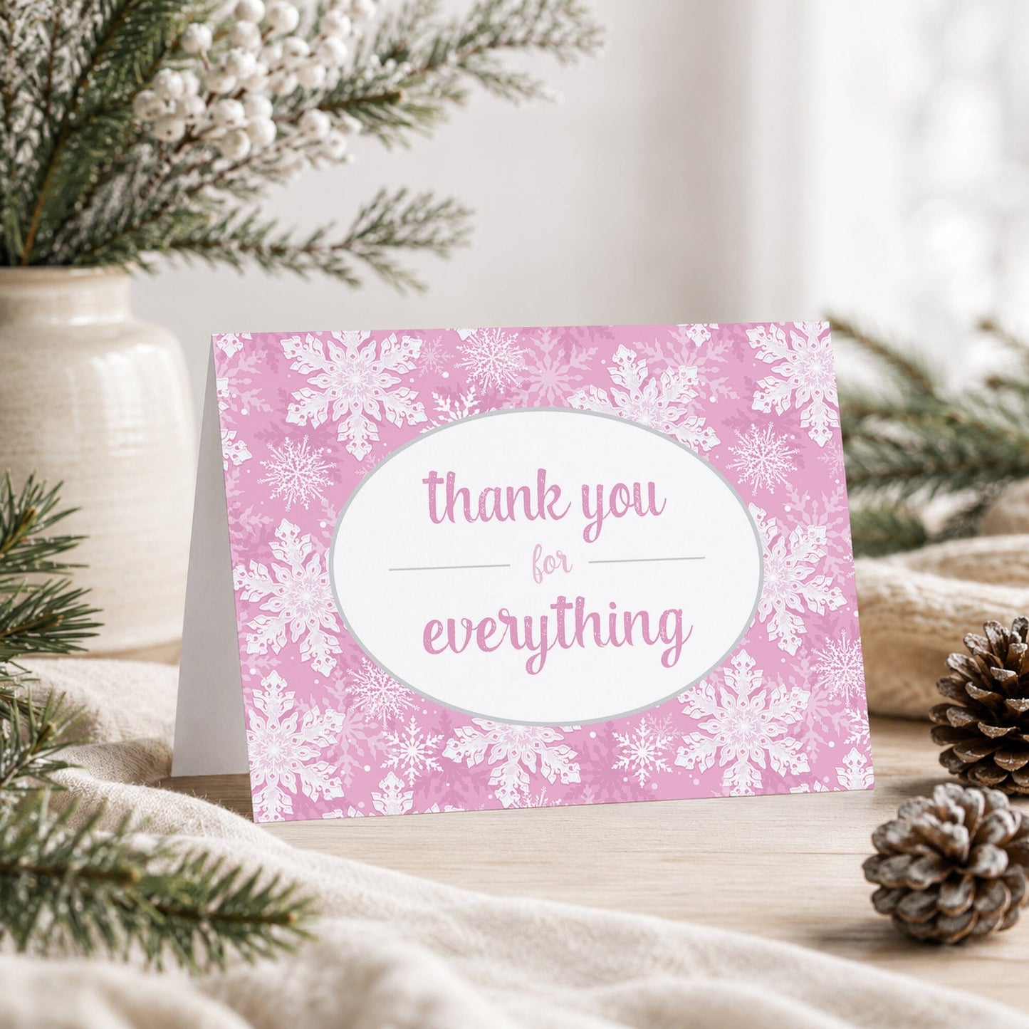 Pink Snowflake Winter Thank You Card shown on a tabletop with a vase, winter greenery, and pine cones.