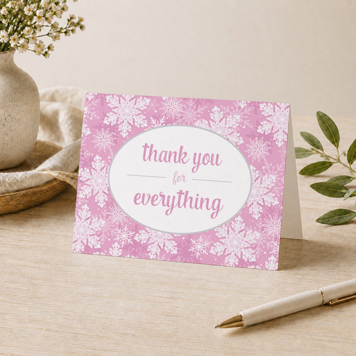 Pink Snowflake Winter Thank You Card shown on a desk with a vase, plants, and a pen.