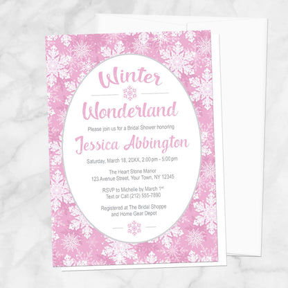 Pink Snowflake Winter Wonderland Bridal Shower Invitation shown on a marble surface with a white envelope.
