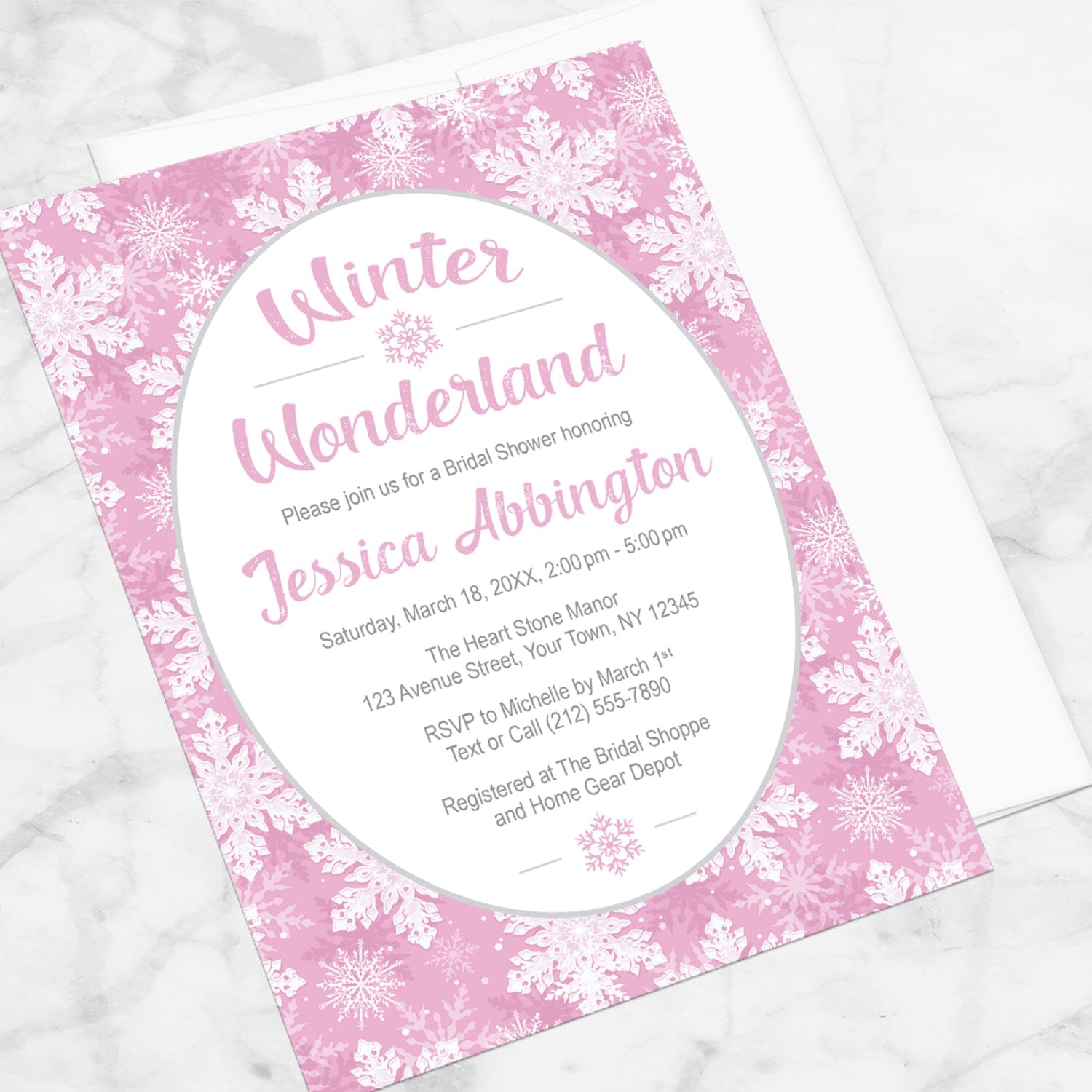 Pink Snowflake Winter Wonderland Bridal Shower Invitation shown at an angle on a marble surface with a white envelope.