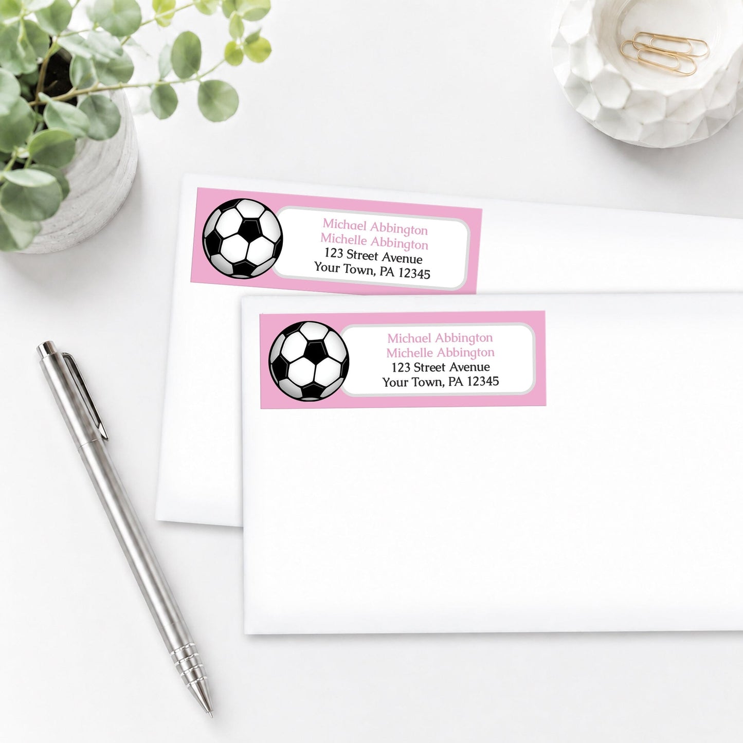 Pink Soccer Ball Address Labels on white envelopes, shown on a white surface with a plant and a pen.