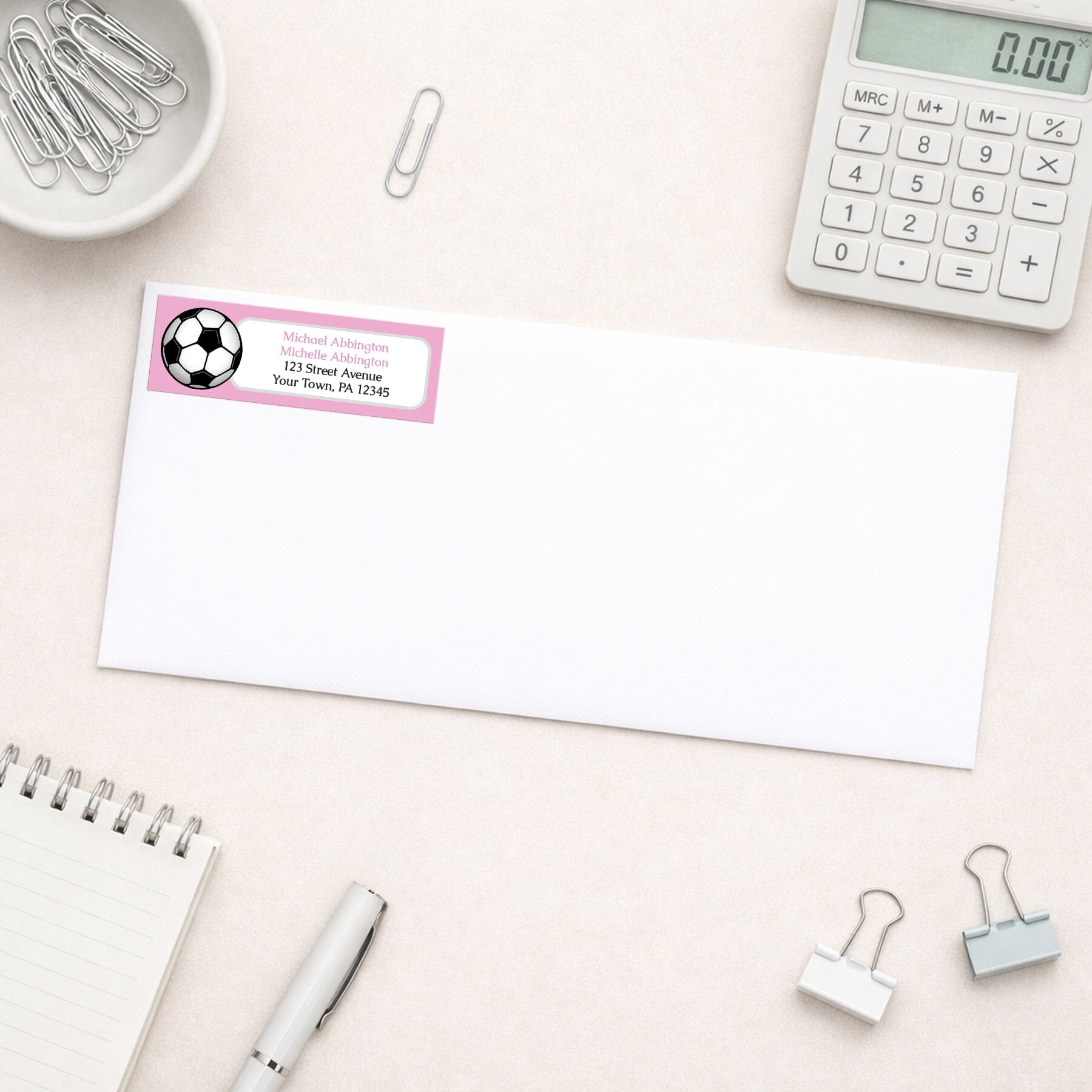 Pink Soccer Ball Return Address Label shown on a white envelope with everyday office supplies