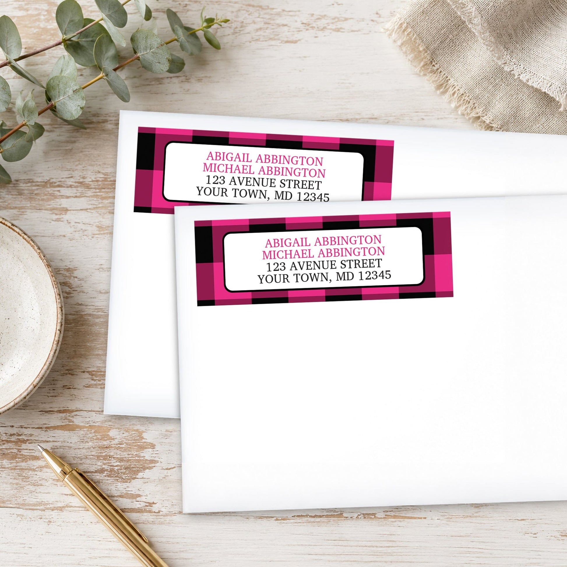 Pink and Black Buffalo Plaid Address Labels on white envelopes, shown on a wooden surface with plants and a pen.