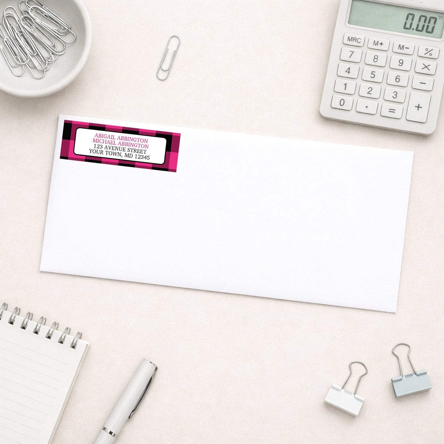 Pink and Black Buffalo Plaid Address Label shown on a white envelope with everyday office supplies