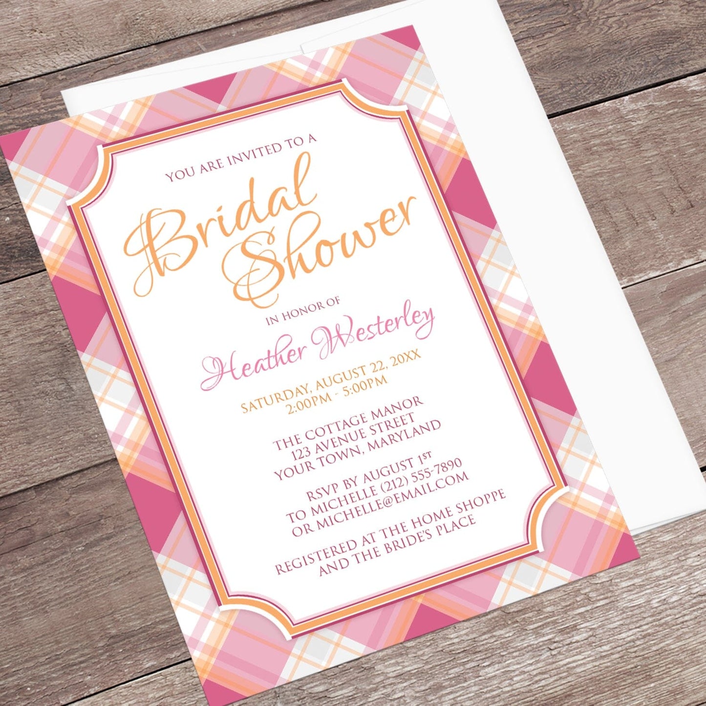 Pink and Orange Plaid Bridal Shower Invitation shown at an angle on a wood surface with a white envelope.