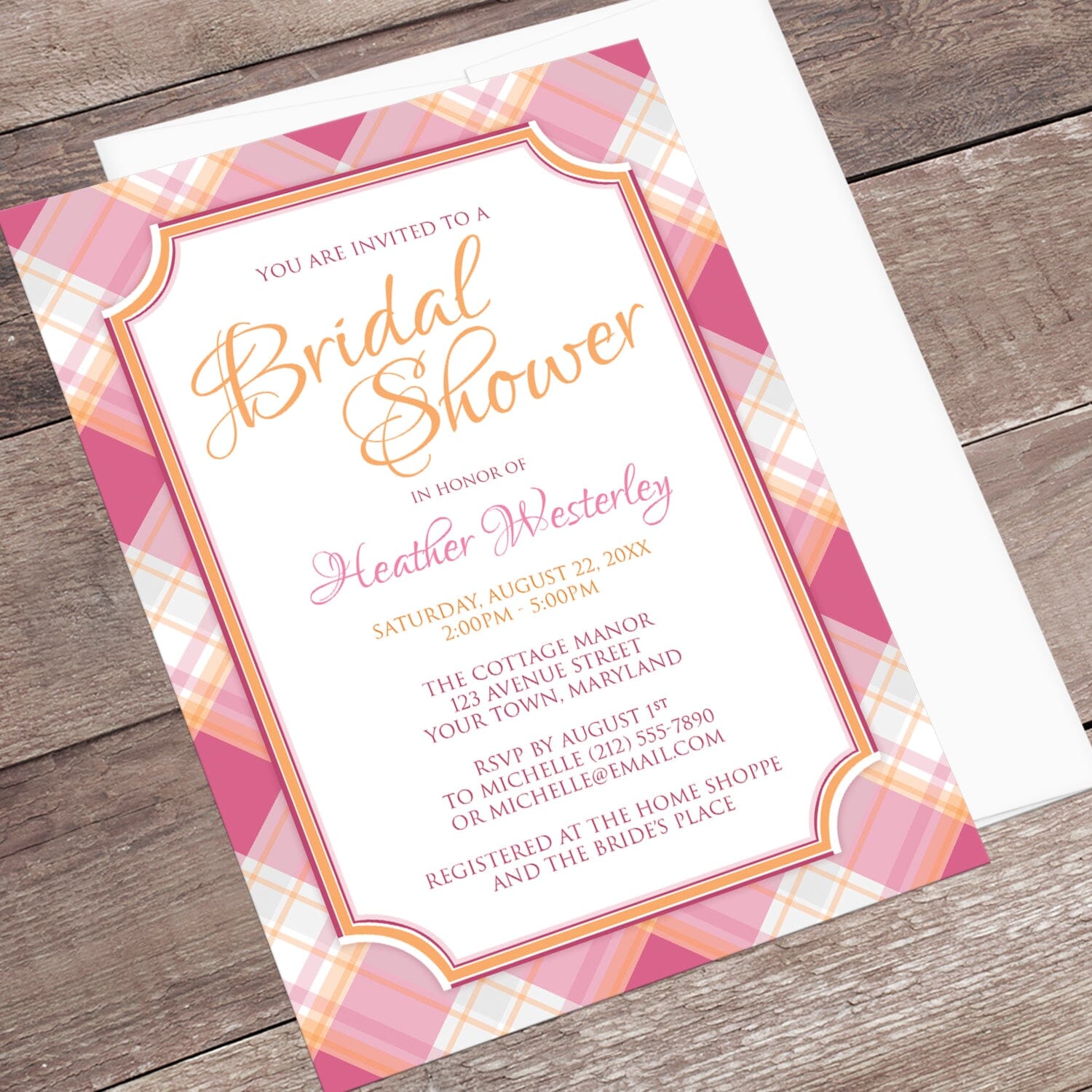 Pink and Orange Plaid Bridal Shower Invitation shown at an angle on a wood surface with a white envelope.