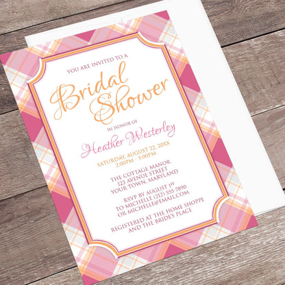 Pink and Orange Plaid Bridal Shower Invitation shown at an angle on a wood surface with a white envelope.