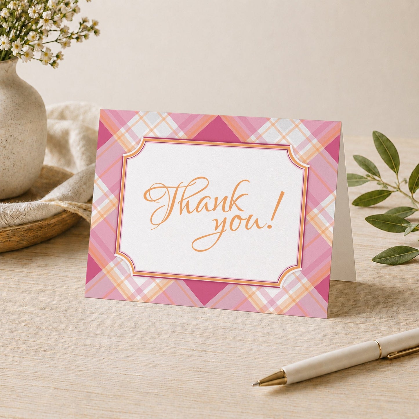 Pink and Orange Plaid Thank You Card shown on a desk with a vase, plants, and a pen.