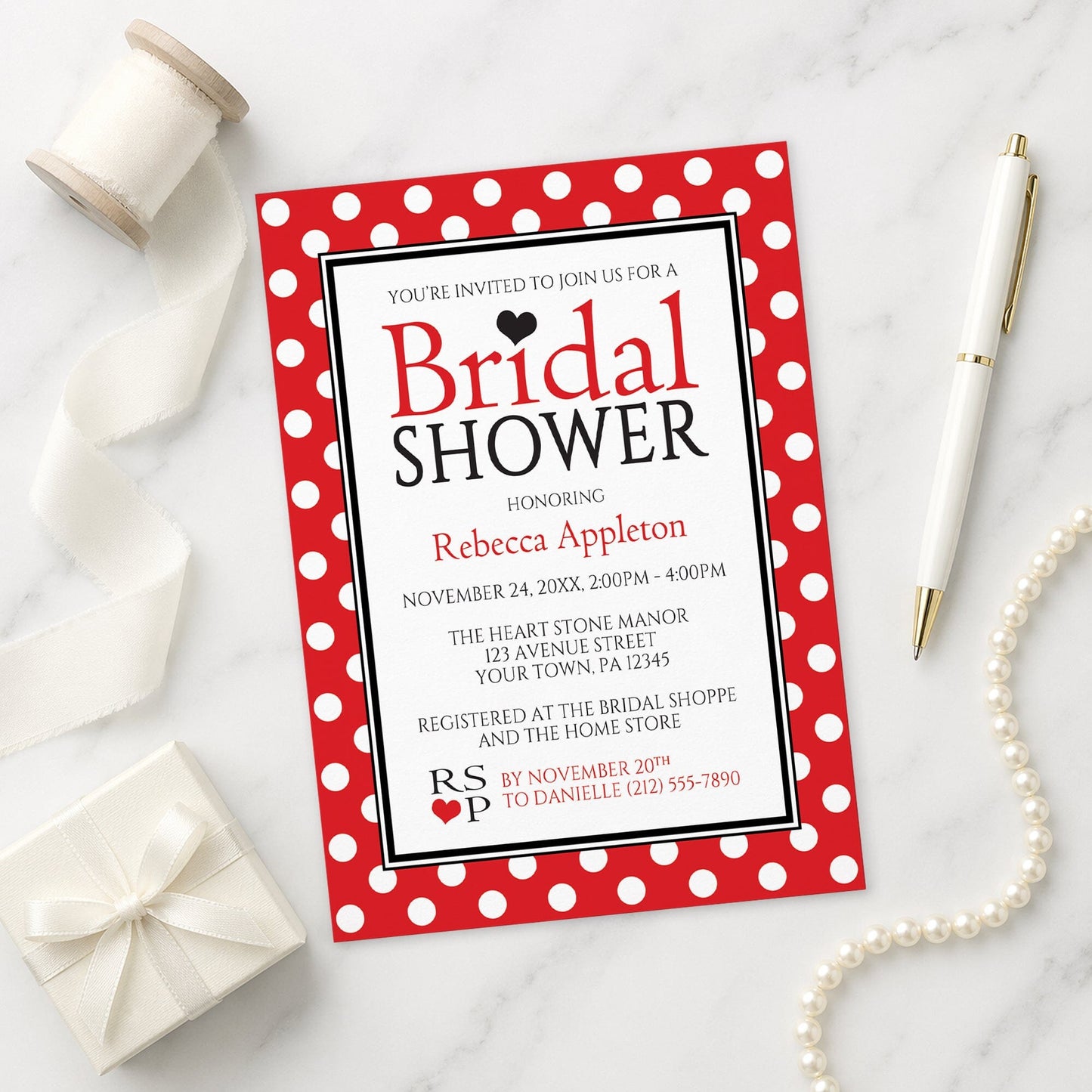 Polka Dot Red Black and White Bridal Shower Invitation shown on a marble surface with a white gift box, pen, ribbon, and pearls.