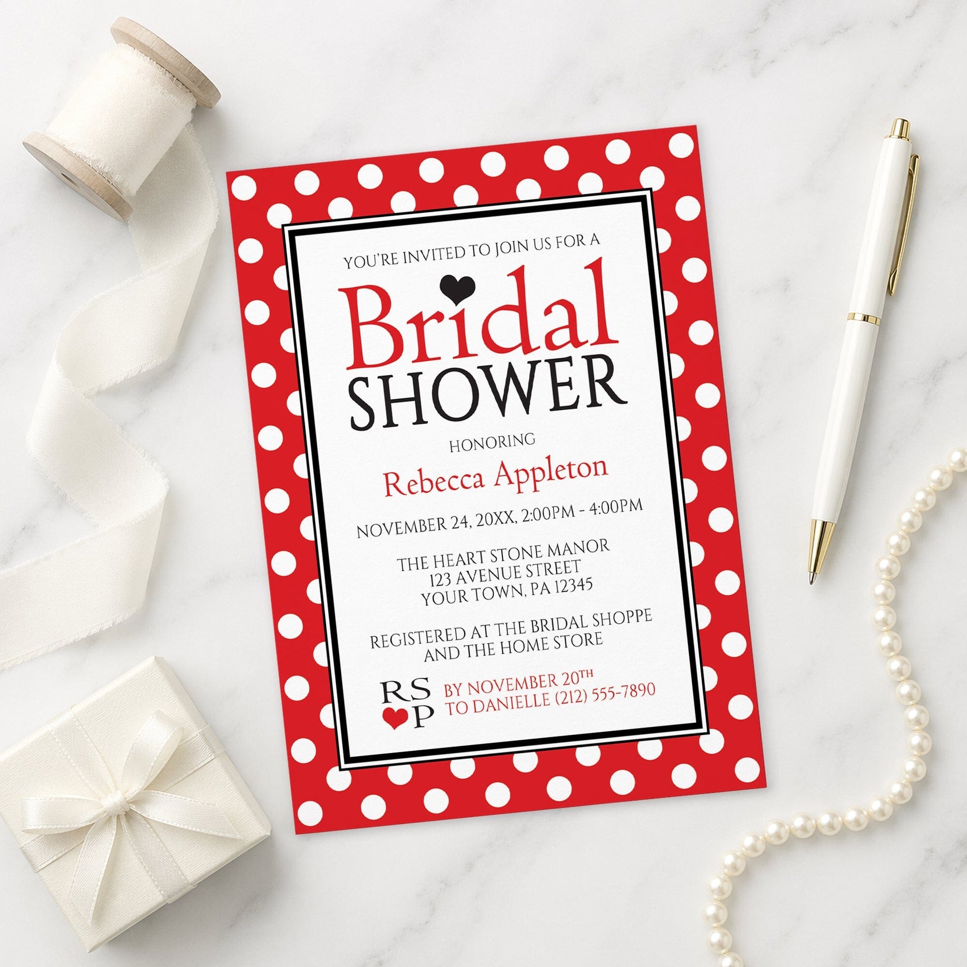 Polka Dot Red Black and White Bridal Shower Invitation shown on a marble surface with a white gift box, pen, ribbon, and pearls.