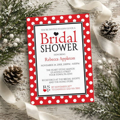 Polka Dot Red Black and White Bridal Shower Invitation shown on a wooden surface with winter greenery, pine cones, and ribbons.