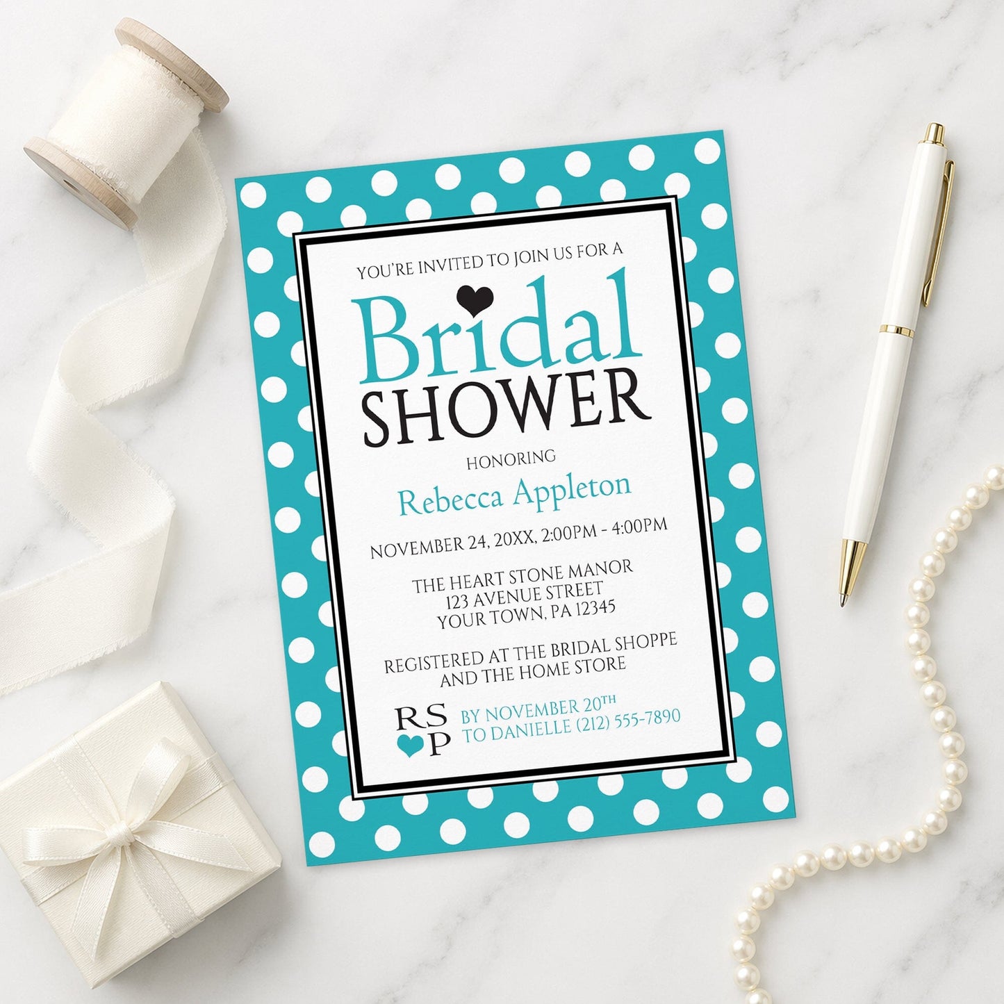 Polka Dot Turquoise Black and White Bridal Shower Invitation on a marble surface with a white gift box, pen, ribbon, and pearls.