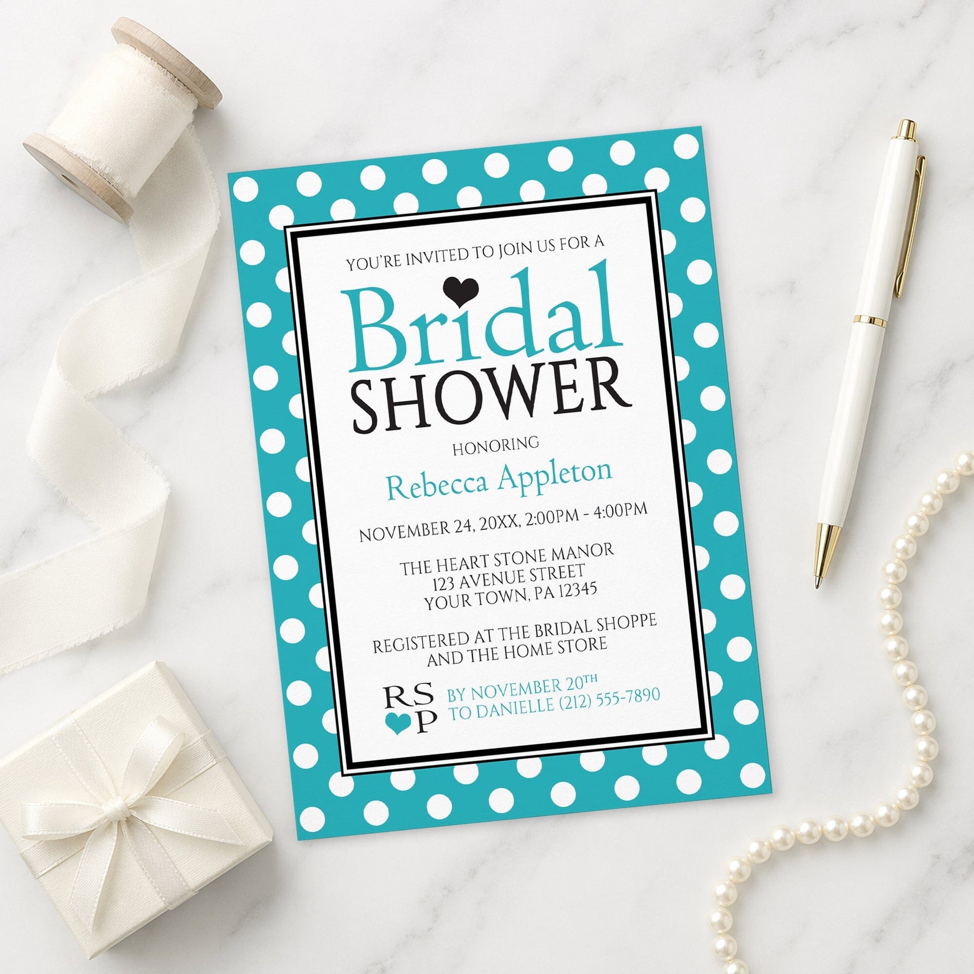 Polka Dot Turquoise Black and White Bridal Shower Invitation on a marble surface with a white gift box, pen, ribbon, and pearls.