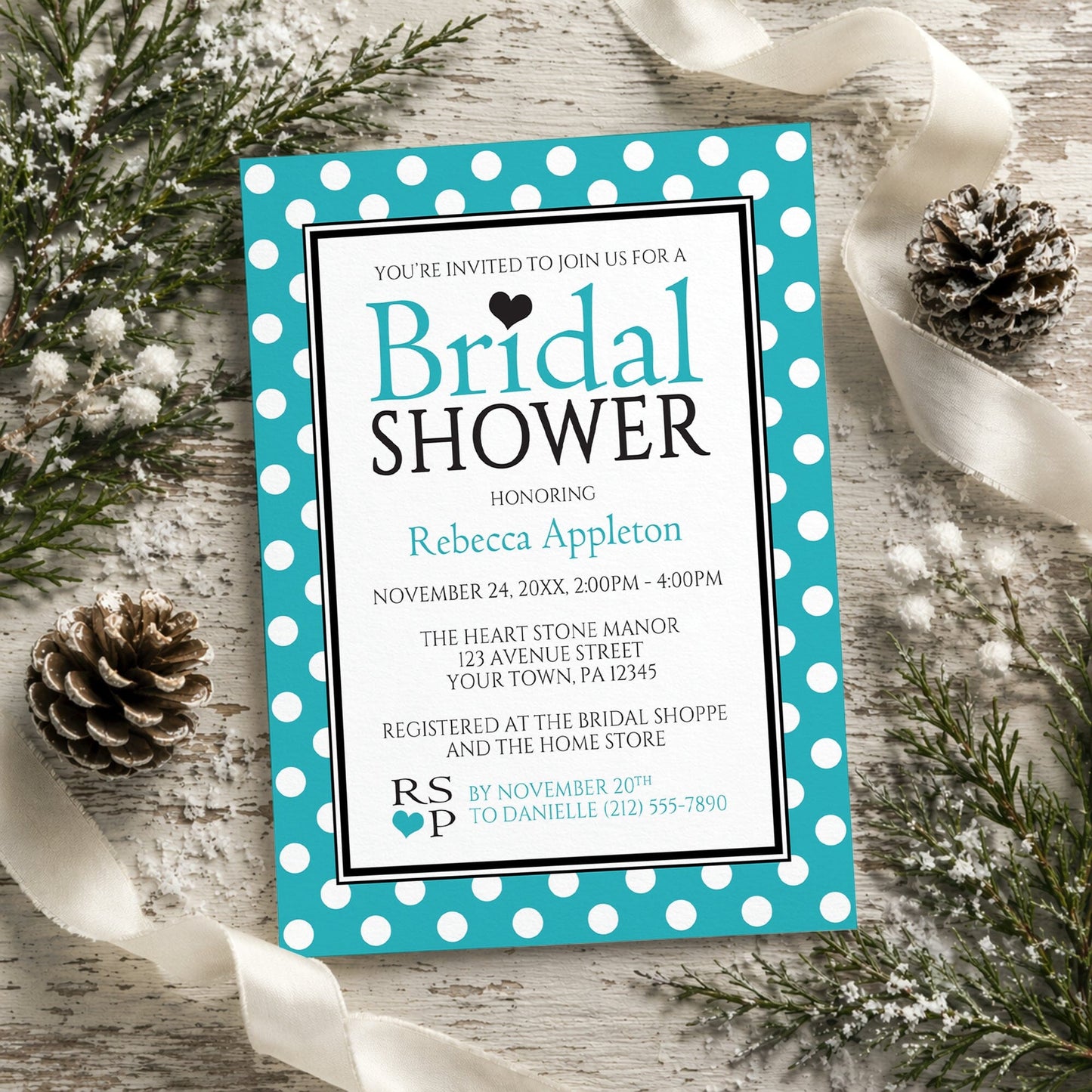Polka Dot Turquoise Black and White Bridal Shower Invitation shown on a rustic wood surface with winter greenery, pine cones, and ribbon.