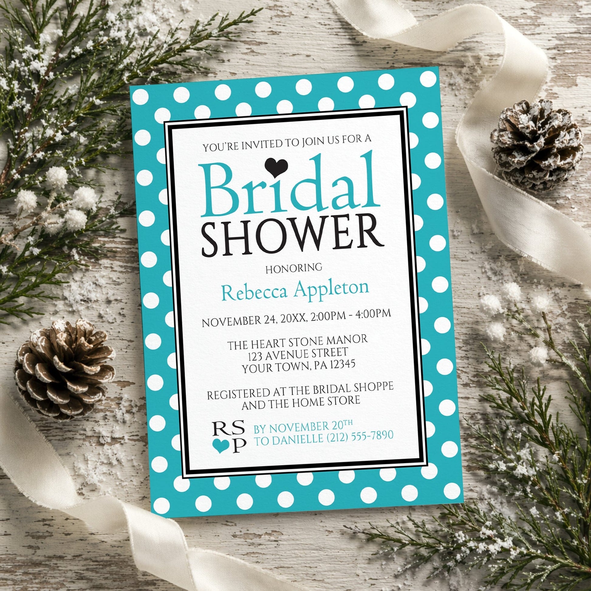 Polka Dot Turquoise Black and White Bridal Shower Invitation shown on a rustic wood surface with winter greenery, pine cones, and ribbon.