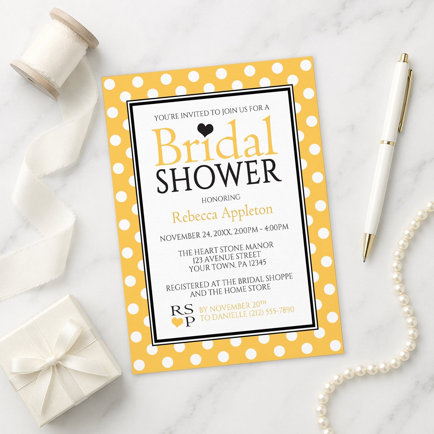 Polka Dot Yellow Black and White Bridal Shower Invitation shown on a marble surface with a white gift box, pen, ribbon, and pearls.