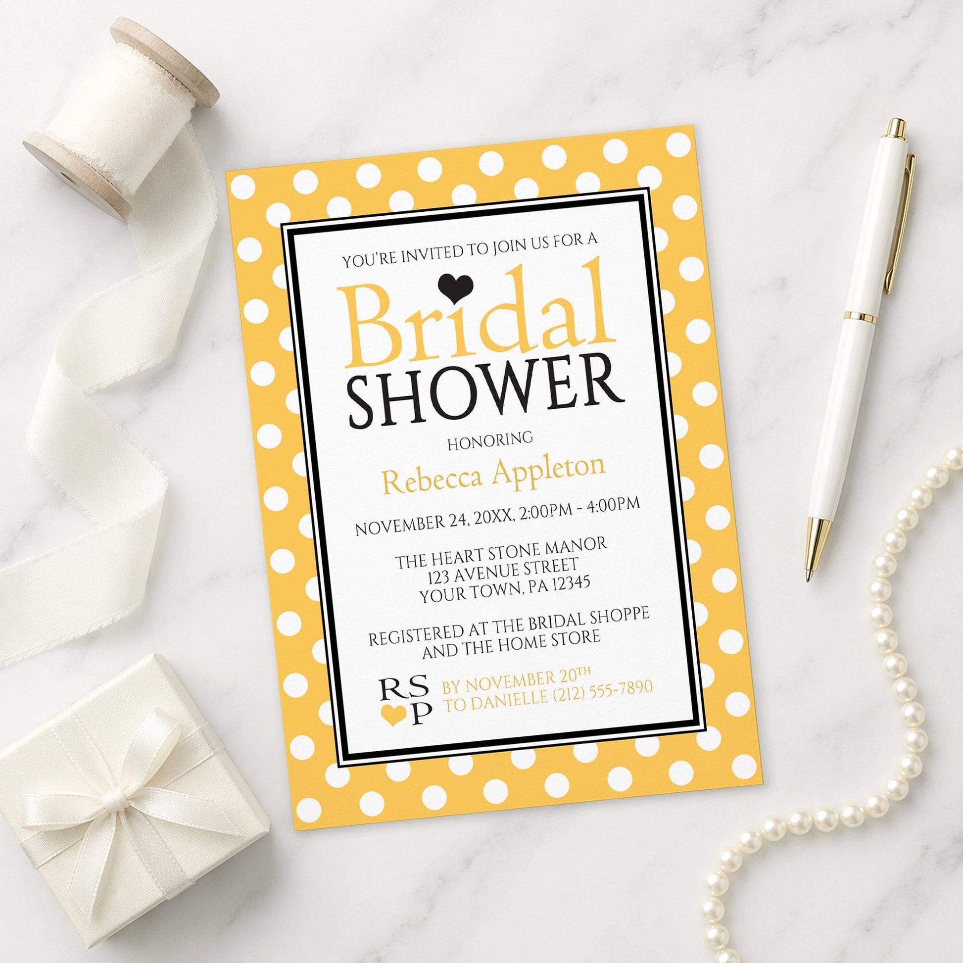 Polka Dot Yellow Black and White Bridal Shower Invitation shown on a marble surface with a white gift box, pen, ribbon, and pearls.