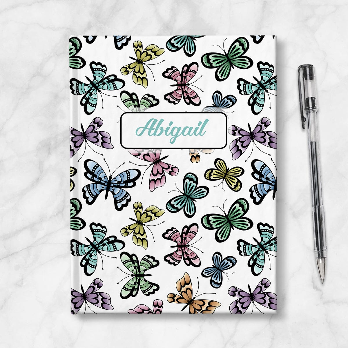 Personalized Pretty Butterflies Pattern Journal at Artistically Invited. Image shows book on a countertop with a pen next to it.