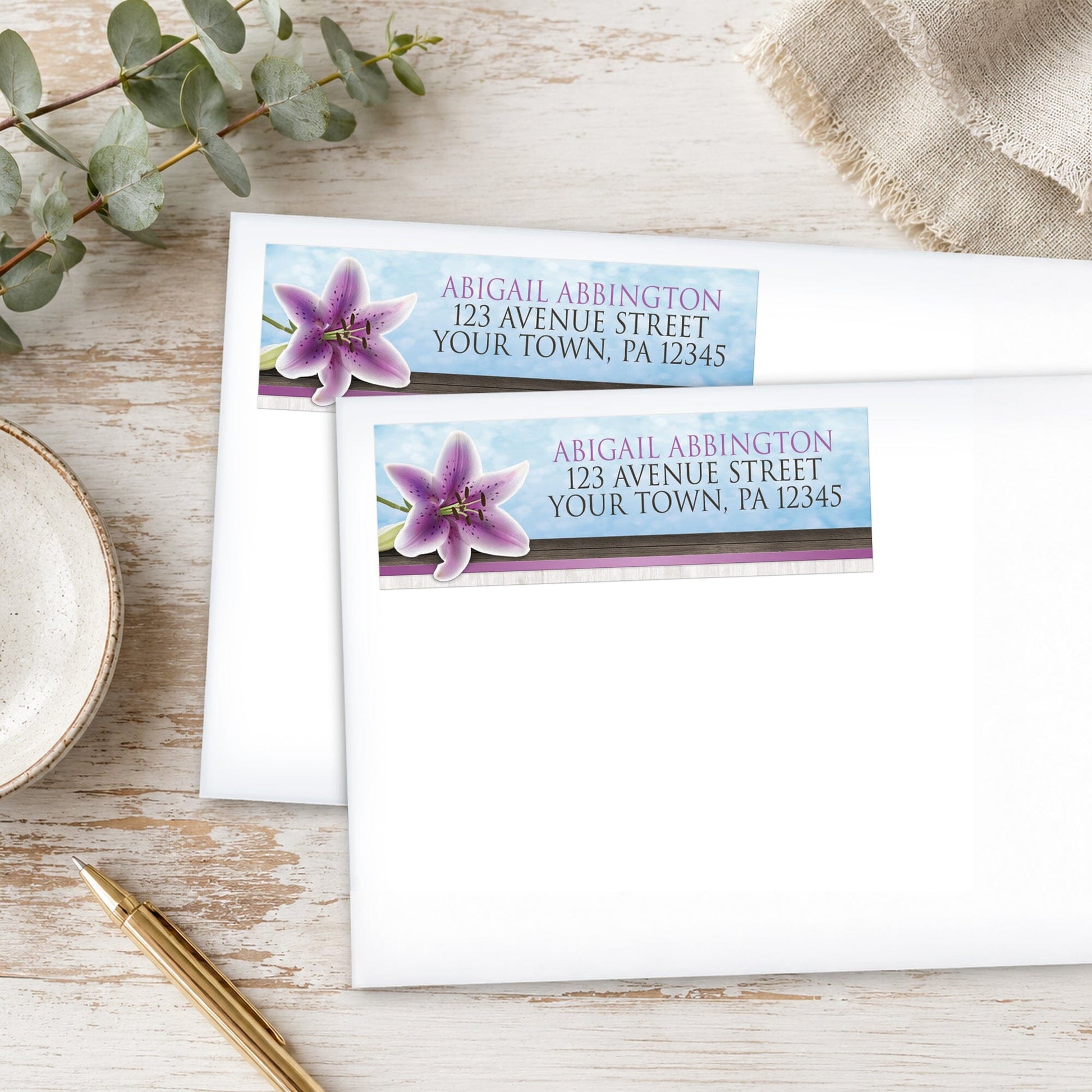 Pretty Floral Wood Purple Lily Address Labels on white envelopes, placed on a wooden surface with eucalyptus leaves and a pen.