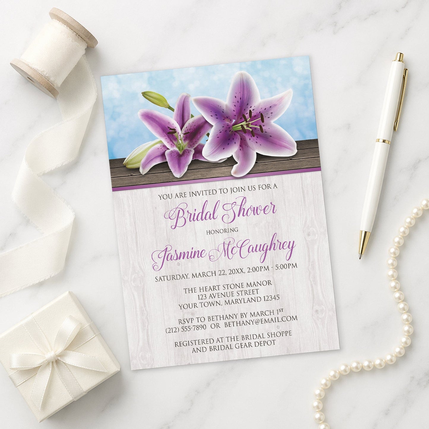 Pretty Floral Wood Purple Lily Bridal Shower Invitation on a marble surface with a pen and gift box.