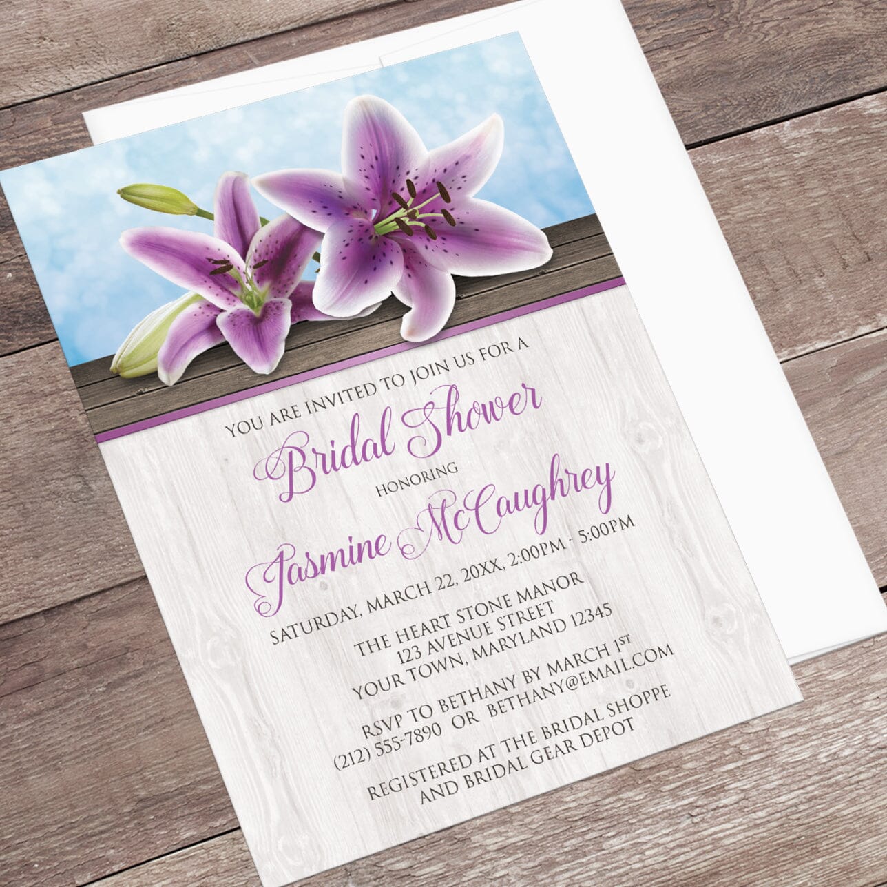 Bridal shower invitation with purple lilies  displayed at an angle with a white envelope on a wooden surface
