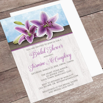 Bridal shower invitation with purple lilies  displayed at an angle with a white envelope on a wooden surface